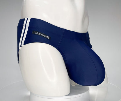 Navy blue WildmanT swim brief with a large pouch, white side stripes, and a brand logo patch on a mannequin.