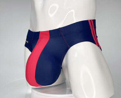 Navy blue swim brief with a prominent red front panel and red side stripes, worn on a white mannequin.