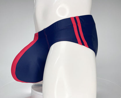 Navy blue and red swim brief with a contoured front pouch and double-stripe detail on a mannequin torso.