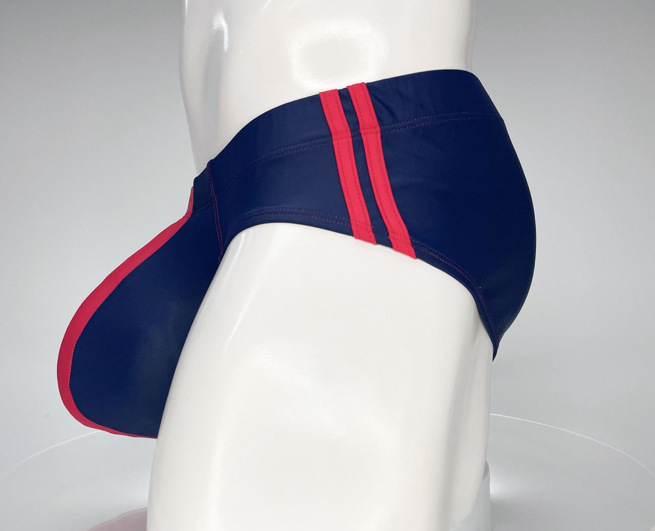 Navy blue swim brief with red trim and dual side stripes on a white mannequin.