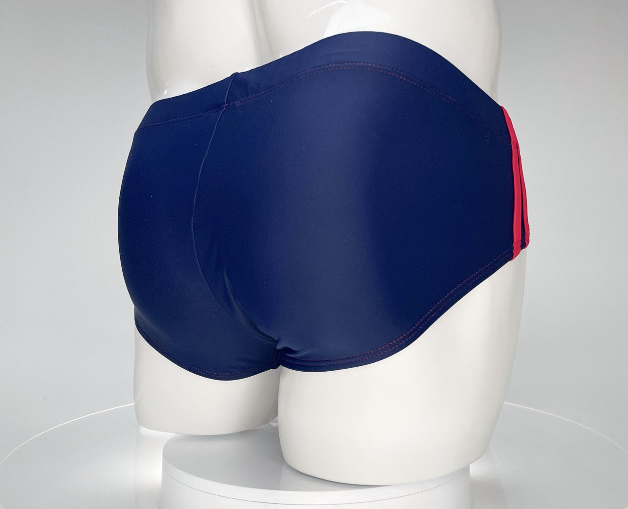 Navy blue swim brief with red side stripes and red stitching, worn on a white mannequin.