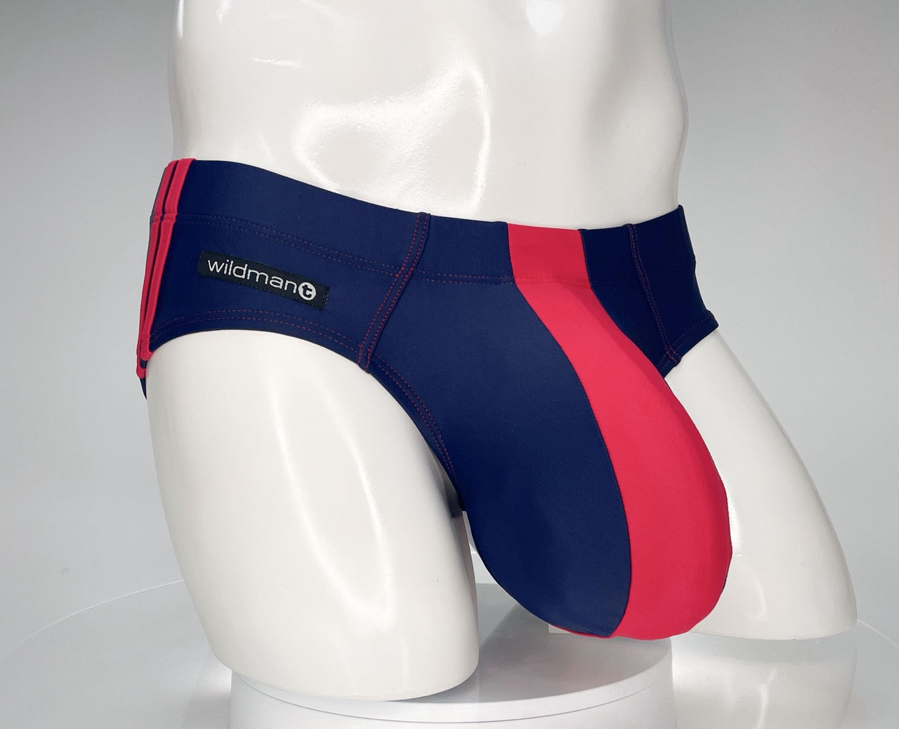 Navy and red WildmanT swim brief with a contoured pouch, red side panel, and side brand logo on a mannequin torso.