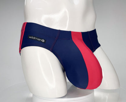 Navy and red WildmanT swim brief with a contoured pouch, red side panel, and side brand logo on a mannequin torso.