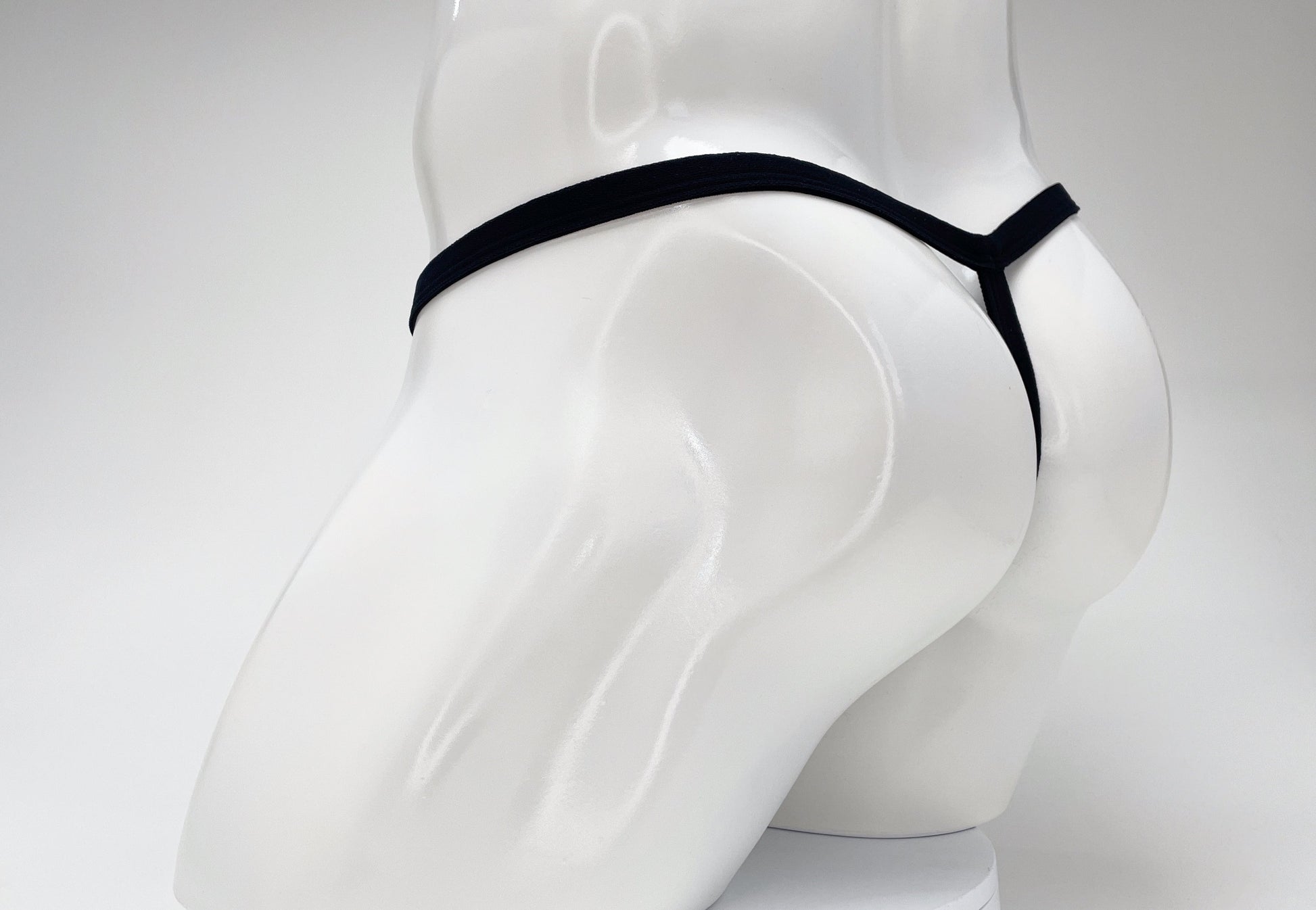 Black thong on a white mannequin torso, seen from behind.