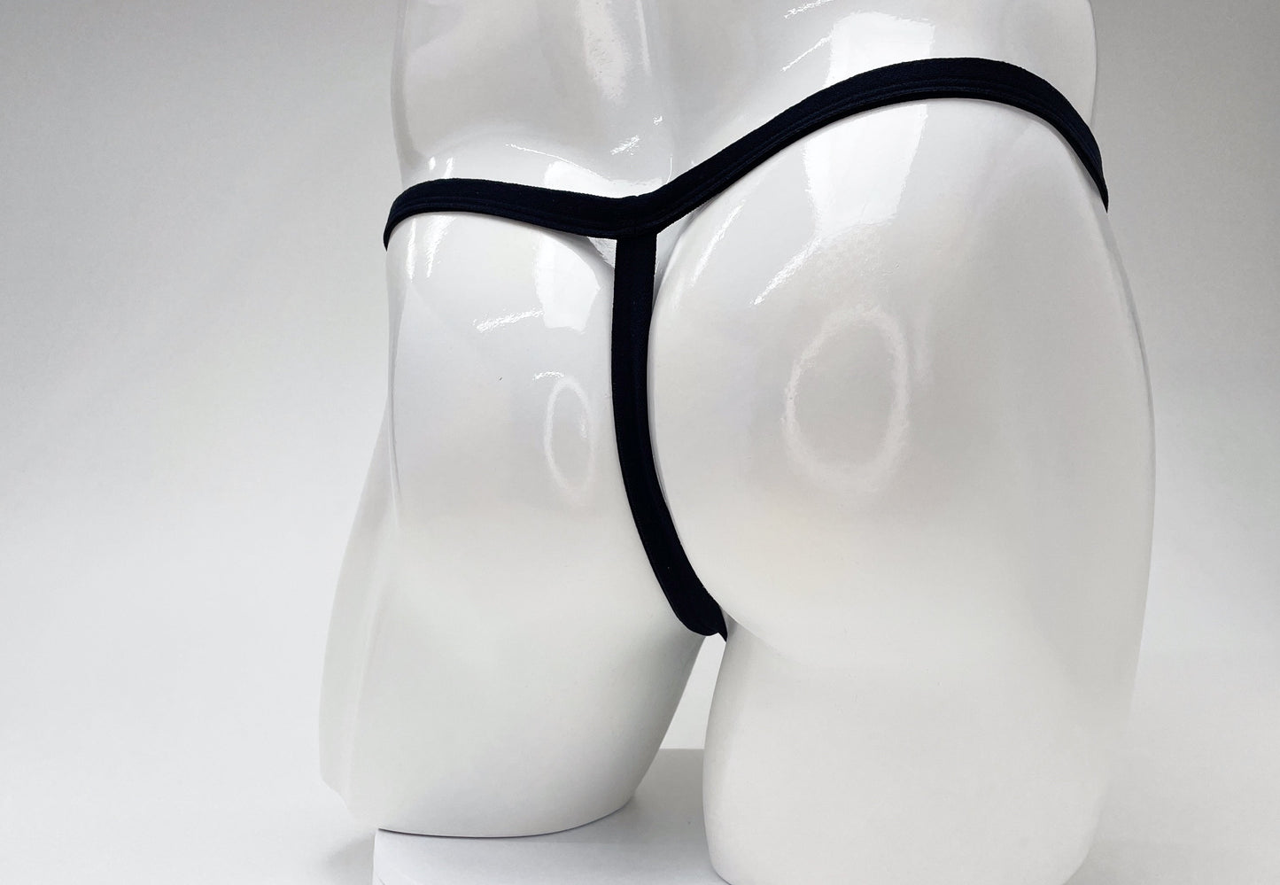Black modal micro thong with a thin waistband and minimalist T-back design on a glossy white mannequin.