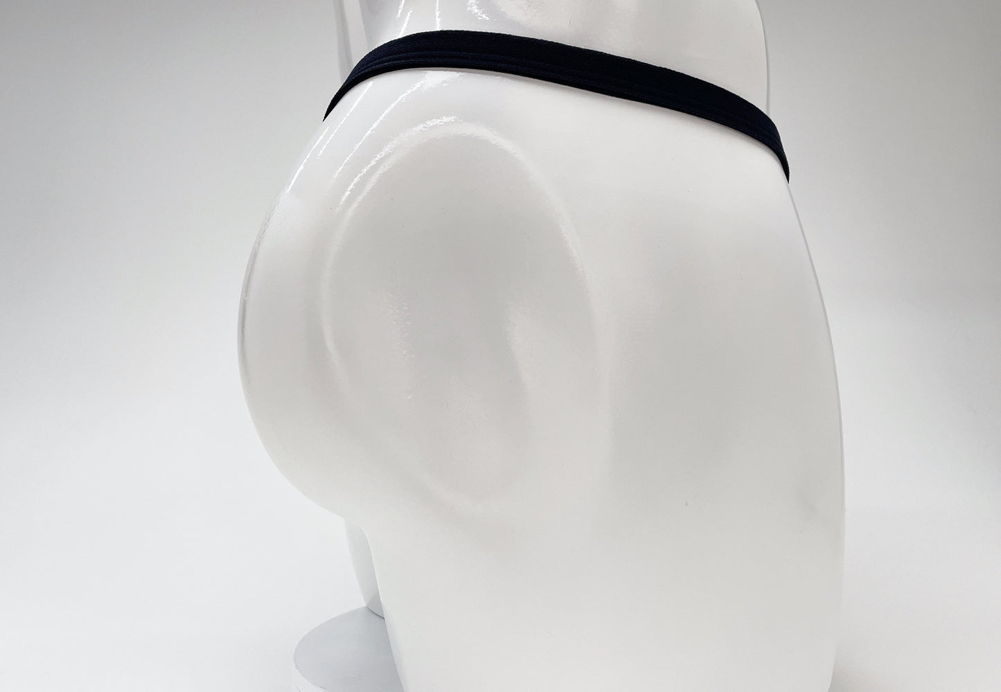 Back view of a gold-colored WildmanT micro thong on a white mannequin, featuring a thin black elastic waistband.