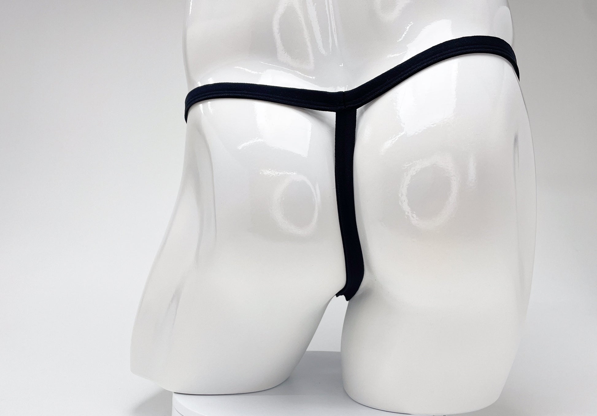 Back view of a white male mannequin wearing a black WildmanT micro thong with thin side straps.