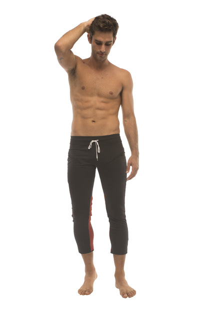 Mens black capri yoga pants with white drawstring and red side panels featuring 4/5 zipper pockets