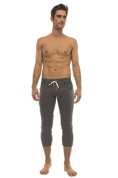 Mens solid charcoal capri yoga pants in stretchy dark gray fabric with white drawstring waistband and zipper pockets