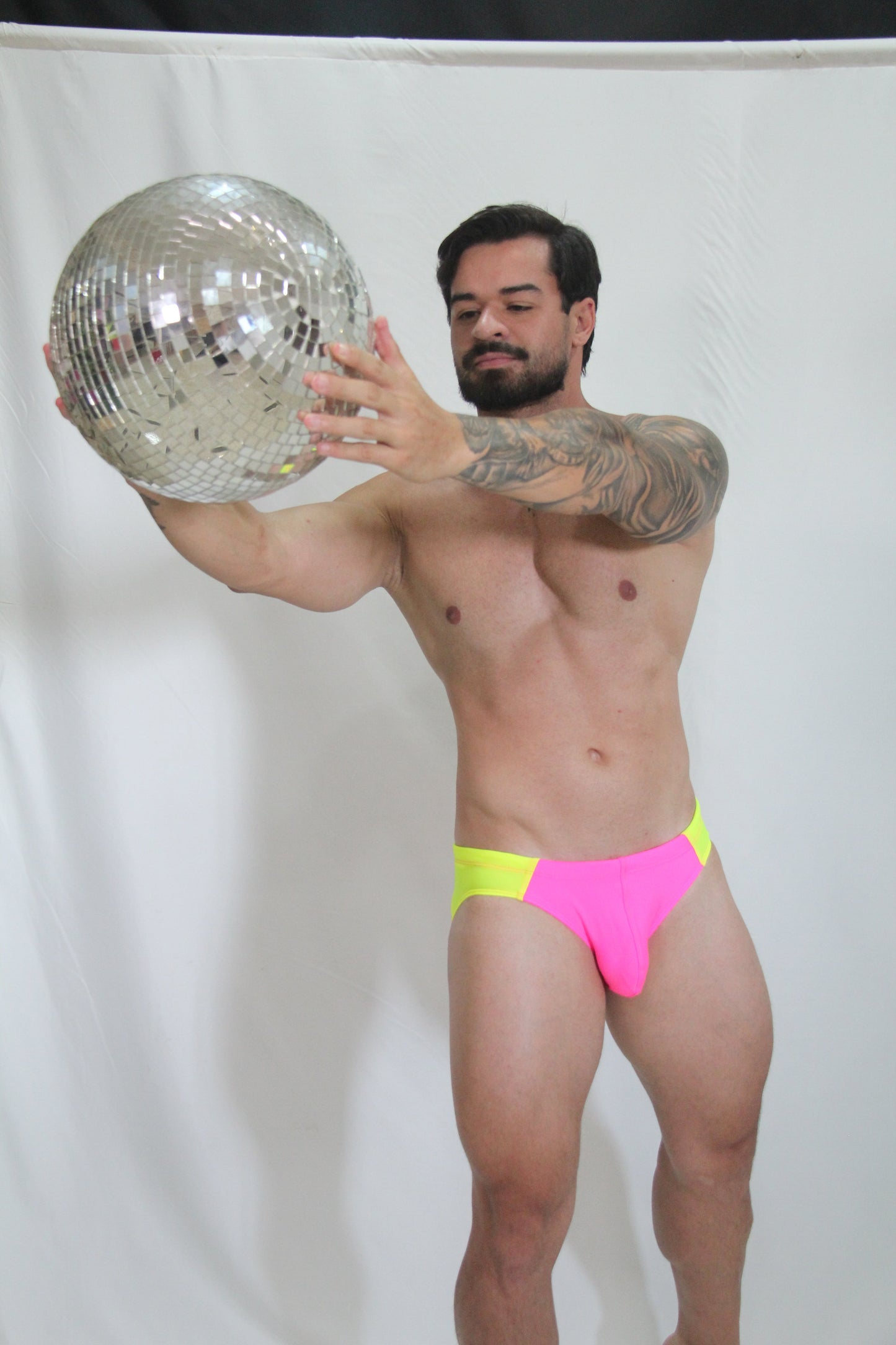 Shiny silver disco ball with mirrored facets reflecting light in a neon curved swim brief product image