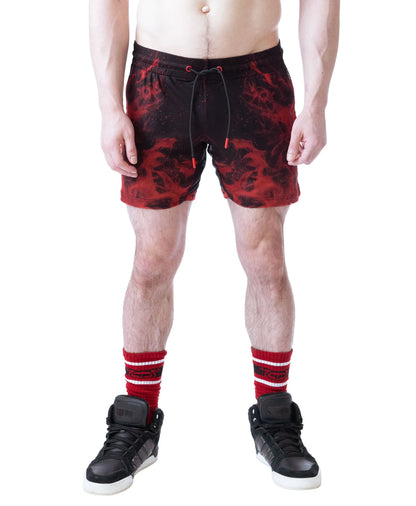 Red and black rugby shorts with a flame pattern worn by a model with a bare torso paired with black sneakers and red-striped socks by Nasty Pig