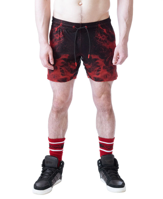 Red and black rugby shorts with a flame pattern worn by a model with a bare torso paired with black sneakers and red-striped socks by Nasty Pig
