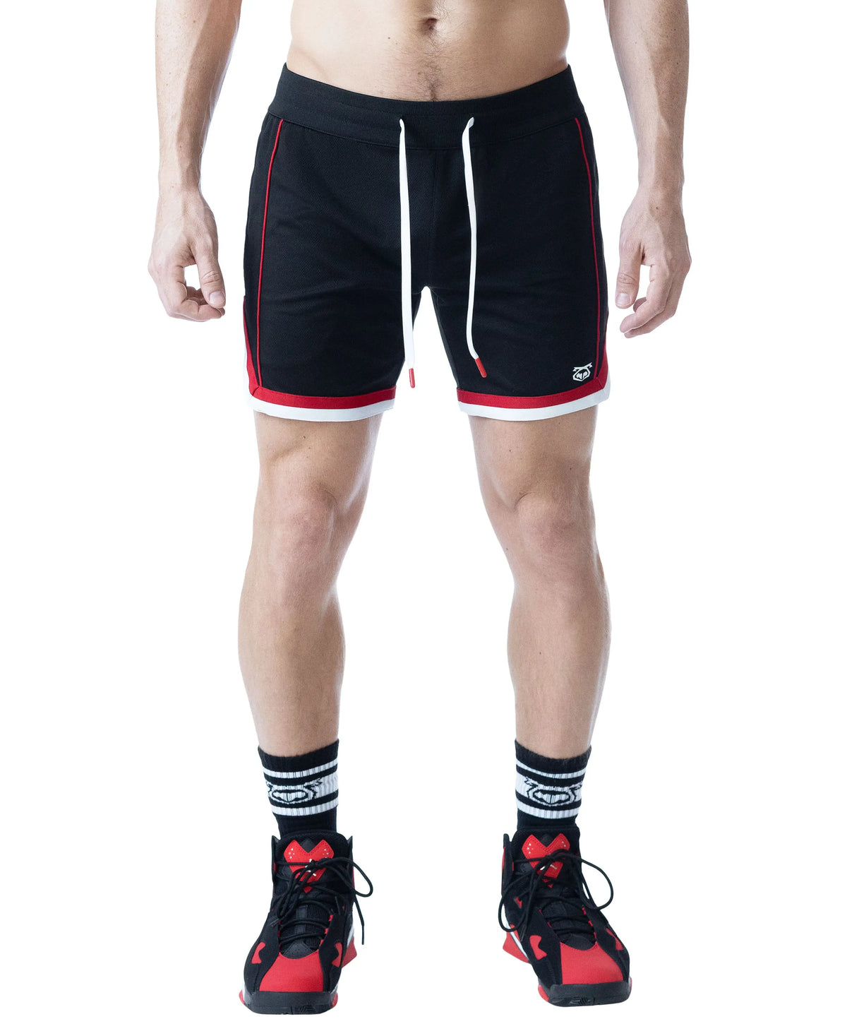 Black rugby shorts with red and white accents featuring a drawstring waist worn by a model with athletic shoes and socks by Nasty Pig
