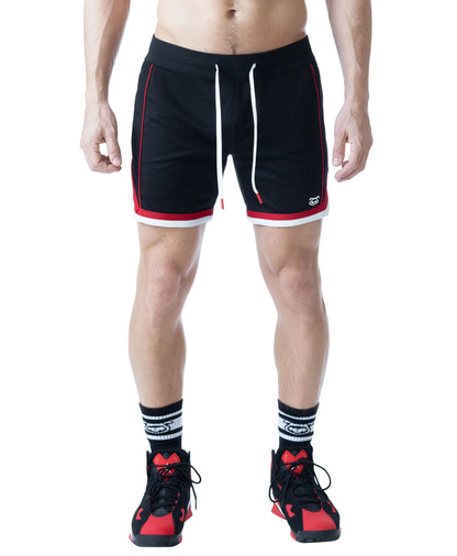 Black rugby shorts with red and white accents featuring a drawstring waist worn by a model with athletic shoes and socks by Nasty Pig