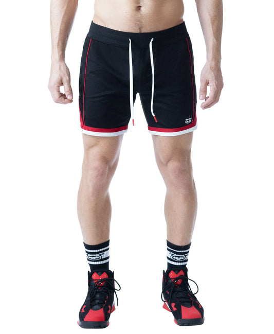 Black rugby shorts with red and white accents featuring a drawstring waist worn by a model with athletic shoes and socks by Nasty Pig