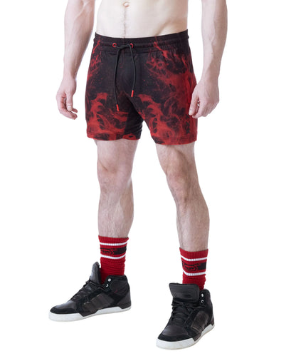Red and black rugby shorts with a flame pattern worn by a model with black sneakers and red striped socks by Nasty Pig