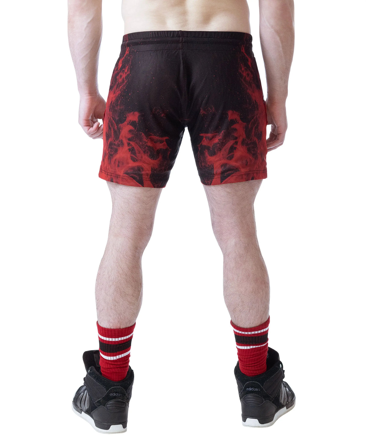 Model wearing black and red rugby shorts with a flame design by Nasty Pig showing the back view and athletic footwear