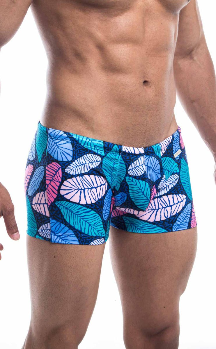 Oceanico square cut swim trunks with vibrant tropical leaf patterns in blue pink and teal on a dark navy base