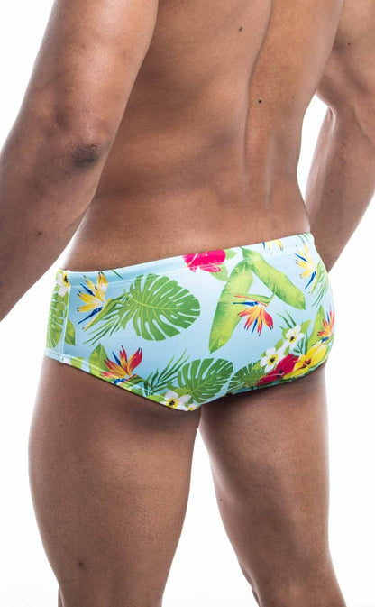 Oceanico swim brief featuring light blue tropical print with green monstera leaves red and yellow bird of paradise flowers and white frangipani blossoms