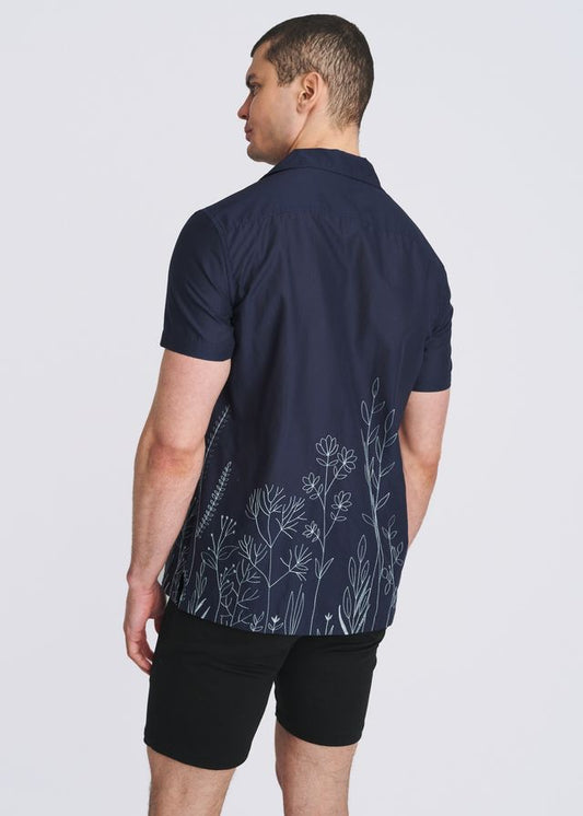 Rear view of a person wearing a navy short-sleeve button-down shirt with light blue embroidered floral hem.