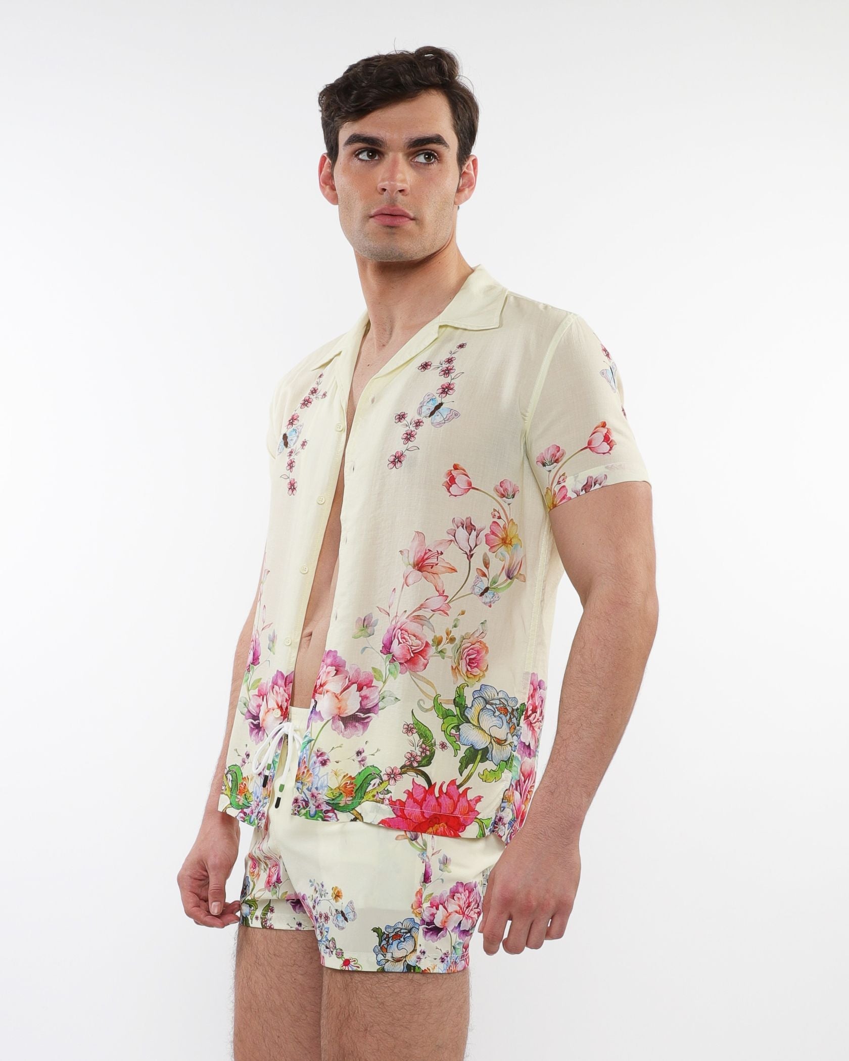 A man wearing a cream printed s/s woven modal border shirt with vibrant floral and butterfly prints