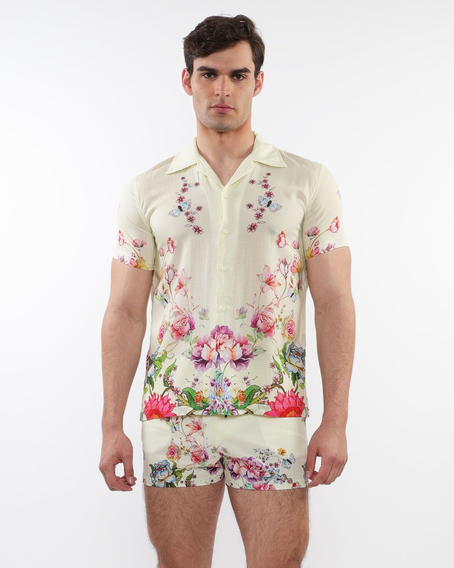 A man wearing a cream printed short sleeve woven modal border shirt with vibrant floral and butterfly patterns