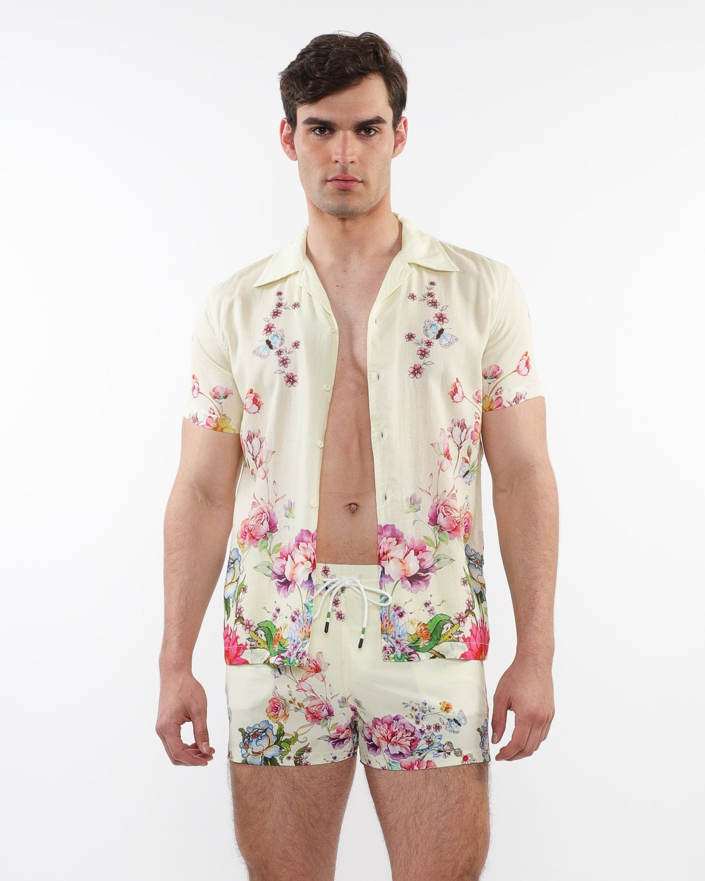 A man wearing a cream printed s s woven modal border shirt and matching shorts with vibrant floral patterns
