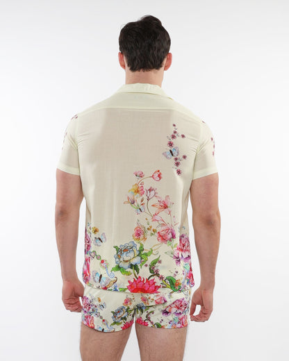 A man wearing a cream printed short-sleeved woven modal border shirt with vibrant floral and butterfly patterns