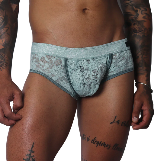 Aqua blue floral lace trunk with solid piping and a contoured pouch, modeled on a tattooed torso.
