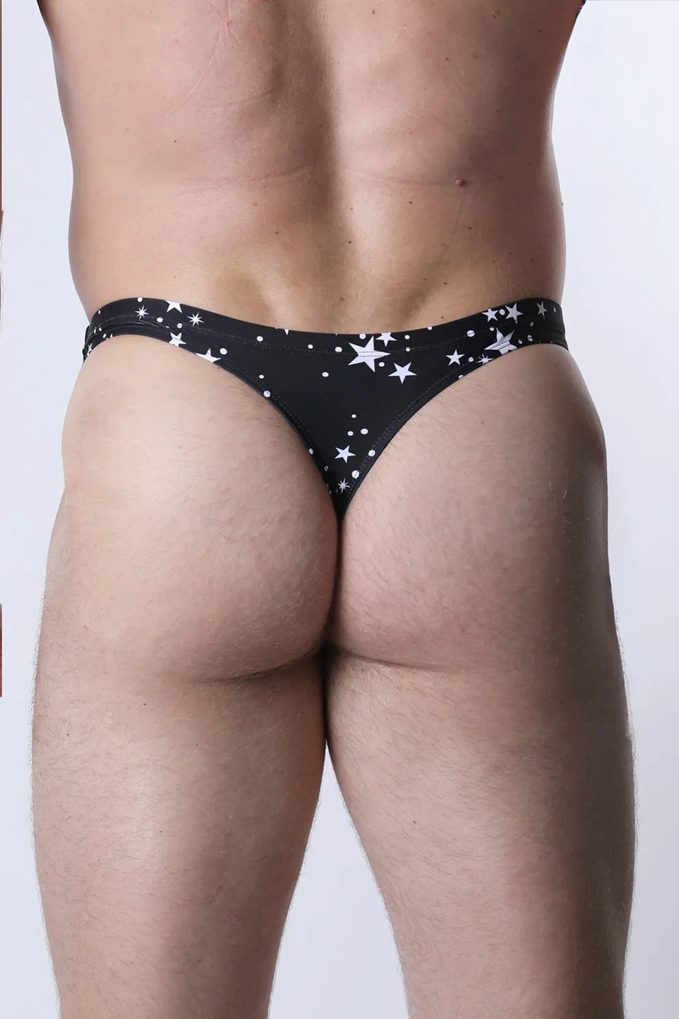 Pulse Swim thong in black fabric with white star patterns of varying sizes scattered across the front side