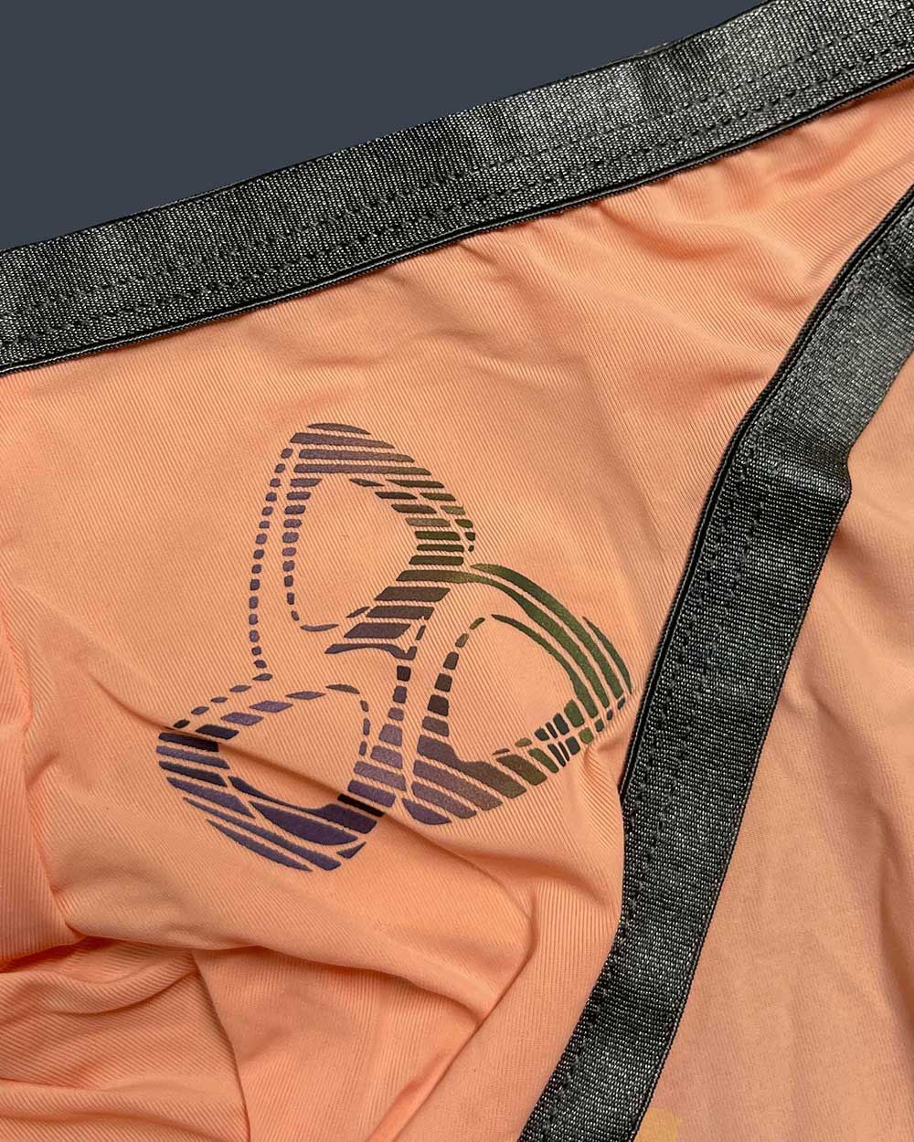 Peach-colored fabric thong with black elastic trim and gradient-striped logo by private structure bare bikini orange