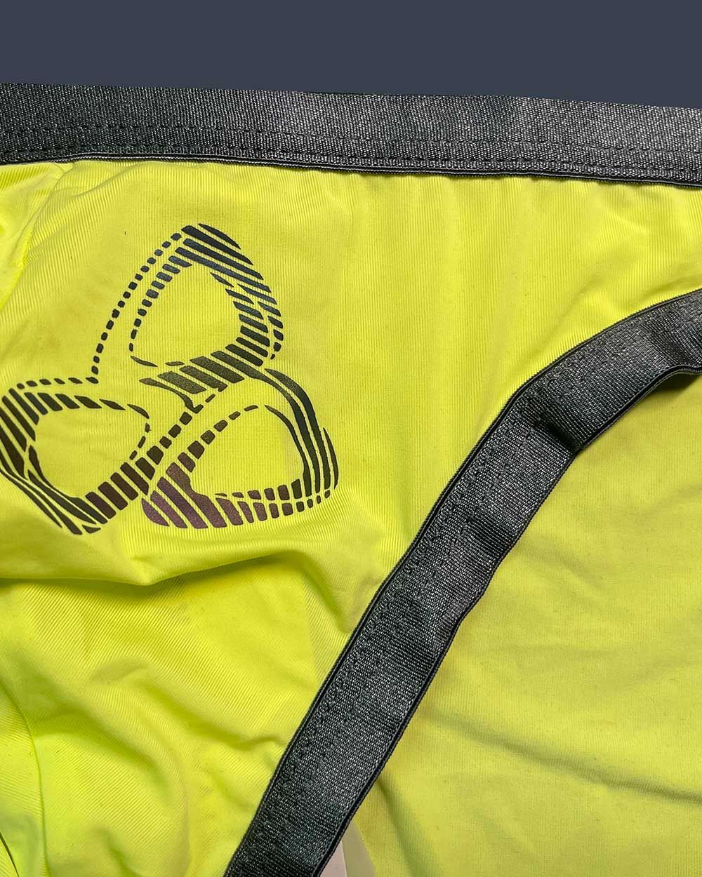 Private Structure BRUT4393 bare bikini briefs in bright yellow with dark gray waistband and black three-leaf logo