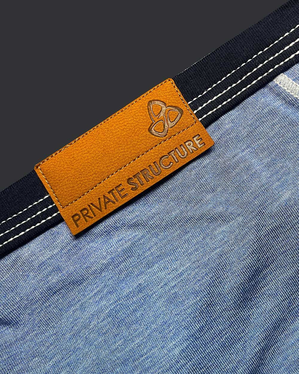 Orange leather brand tag with embossed logo and private structure text on denim fabric of low rise mini brief
