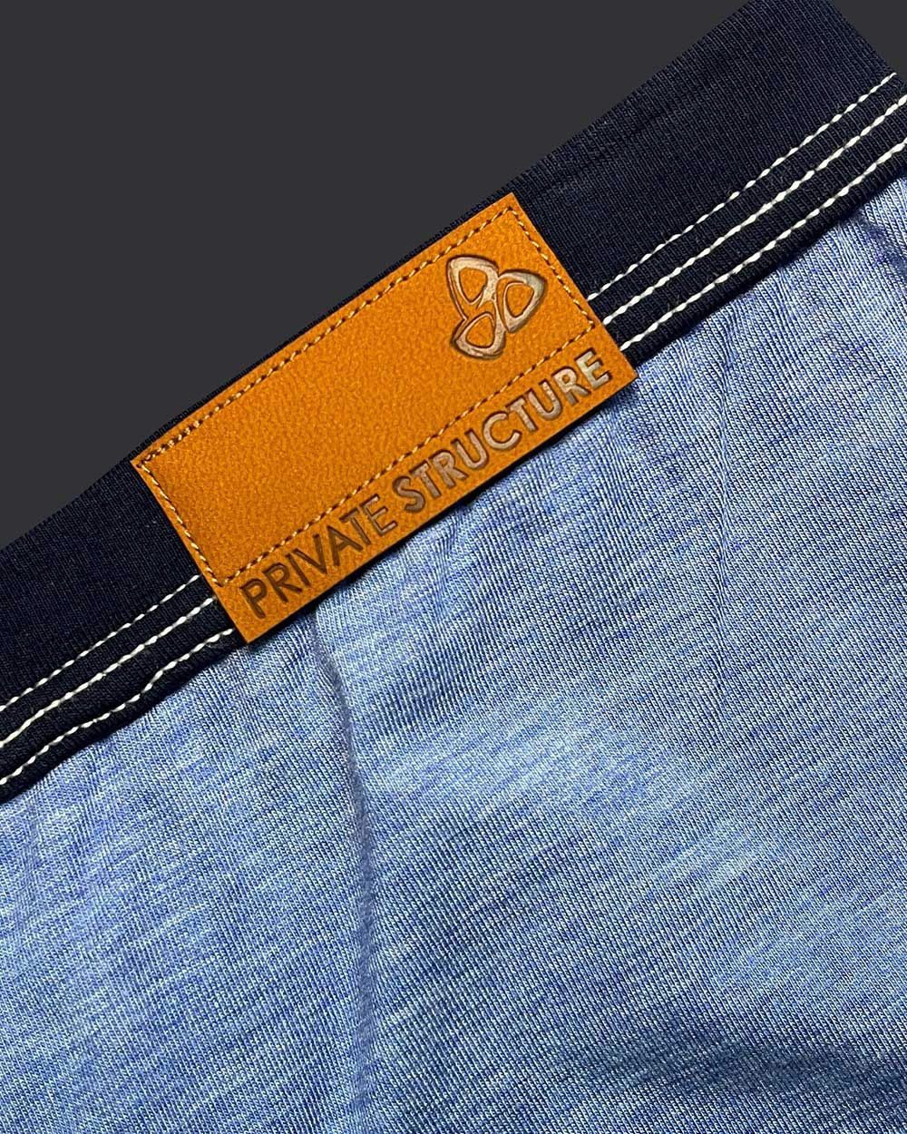 Orange leather brand tag with embossed logo and private structure text on dark blue denim waistband of barn boy low rise trunk