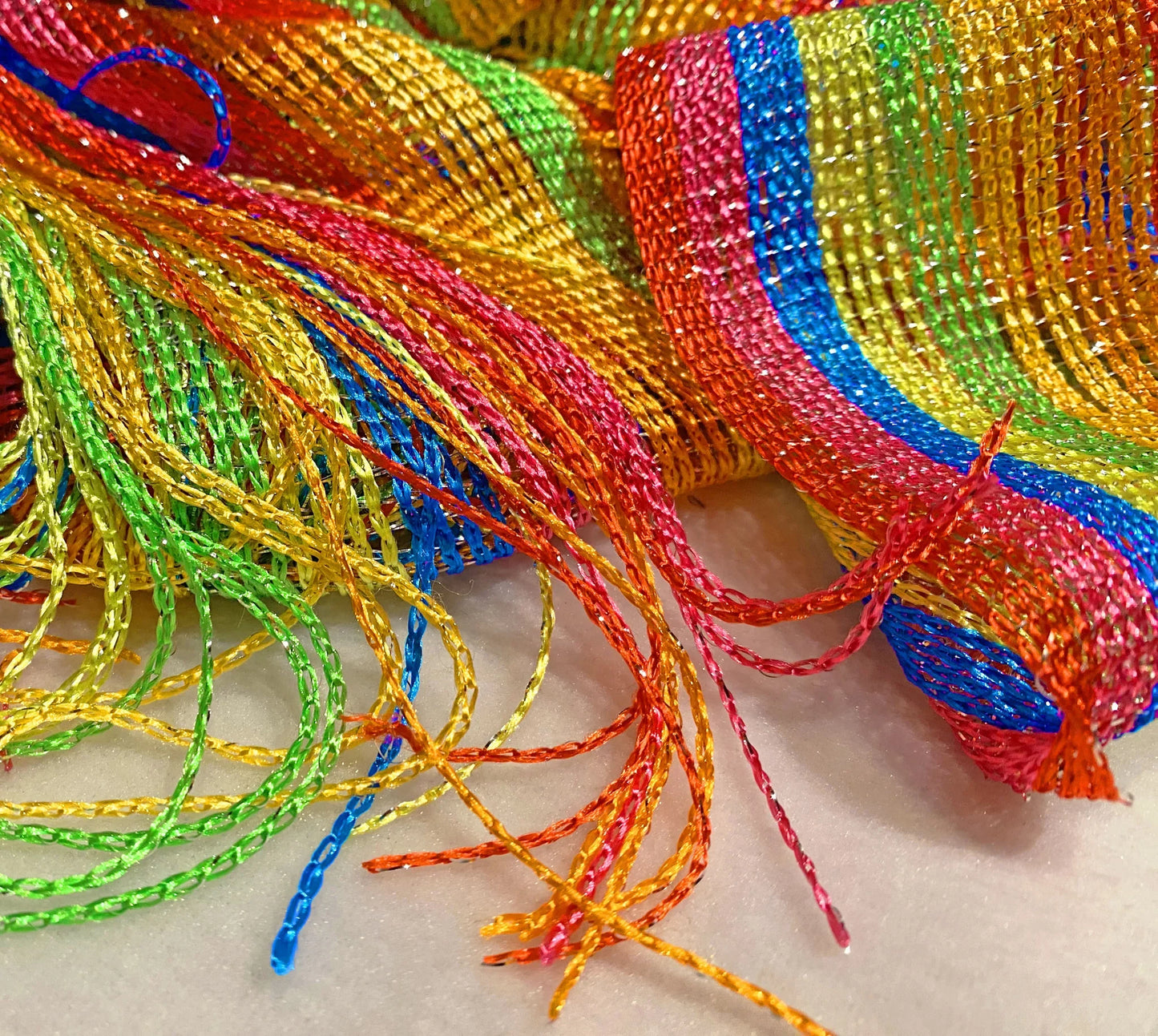Rainbow glitter poncho featuring a woven mesh ribbon with rainbow colors and fringed ends for festive wear