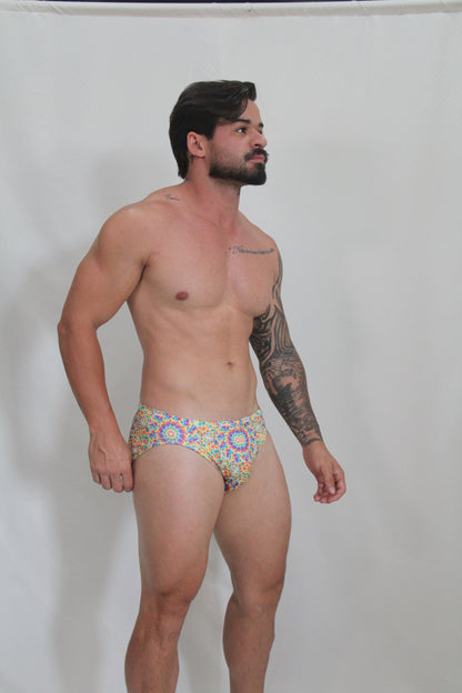 Rainbow kaleidoscope swim brief featuring vibrant blue yellow and red geometric patterned swim trunks front view
