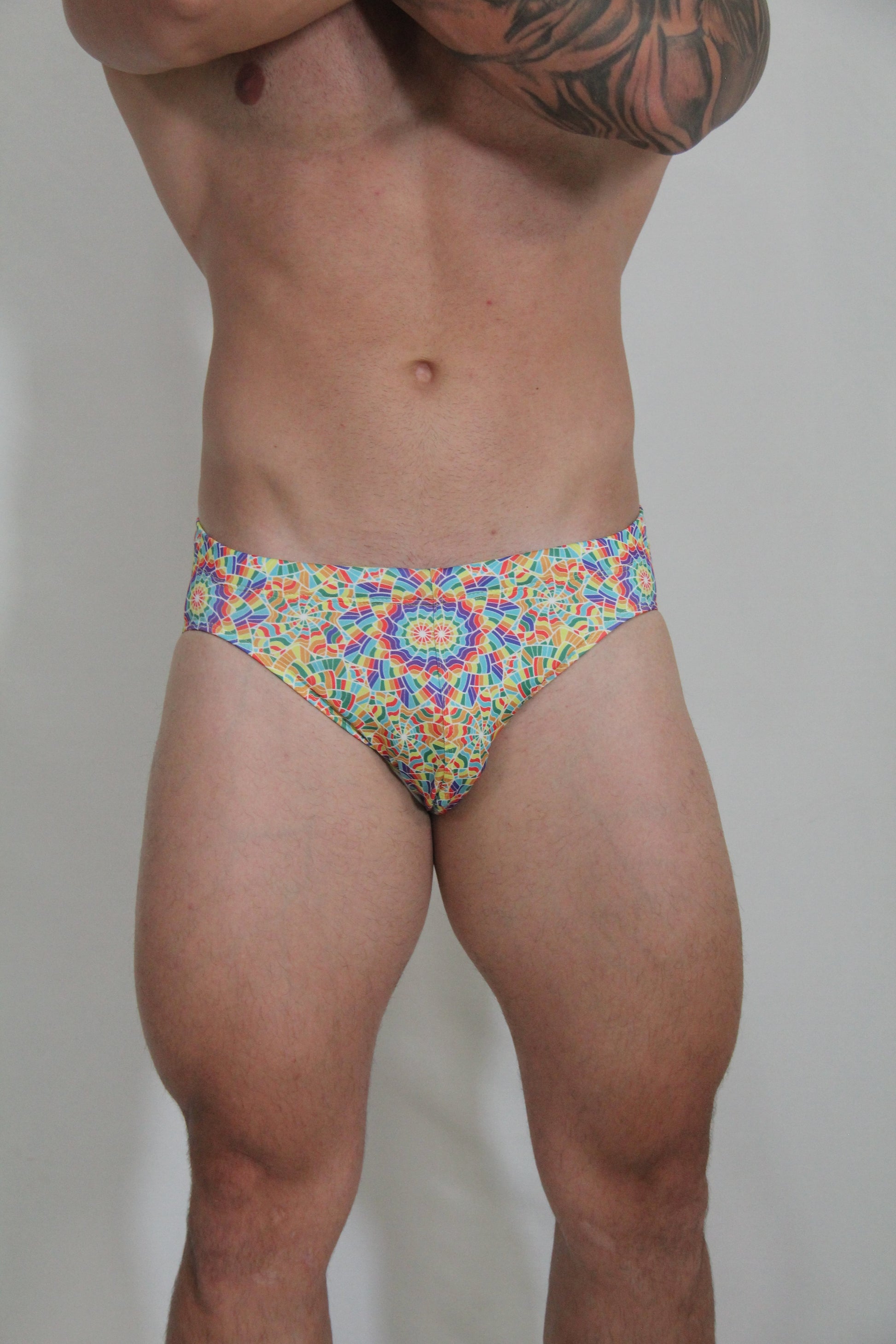 Rainbow kaleidoscope swim brief with vibrant multicolored geometric patterned fabric featuring a bold mandala design