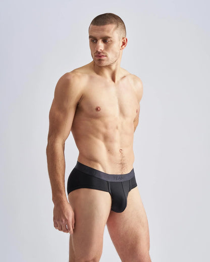 Black men’s REIGN briefs with a dark gray waistband featuring team branding in white lettering for everyday comfort