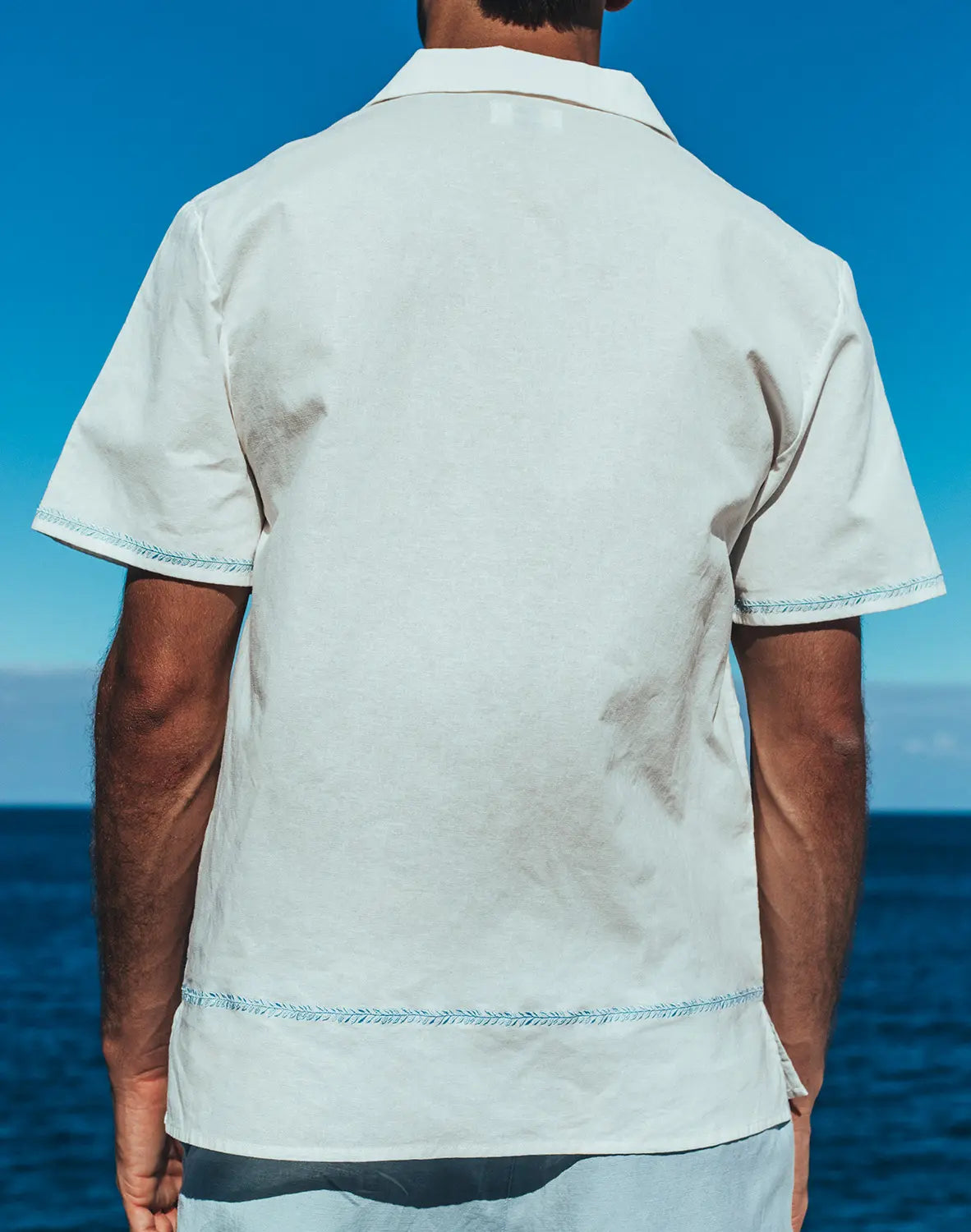 Santorini linen shirt is a crisp white short-sleeved button-up with light blue stitching on hem and sleeve cuffs