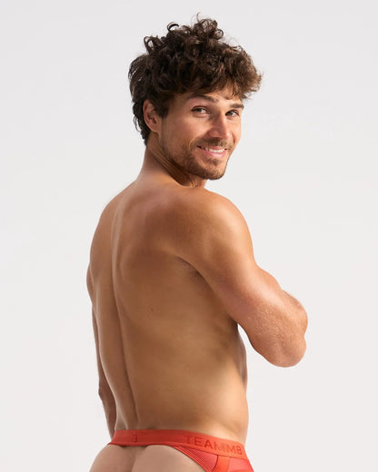 A man wearing bright red calvin klein score sheer jock briefs with a visible logo waistband in front view