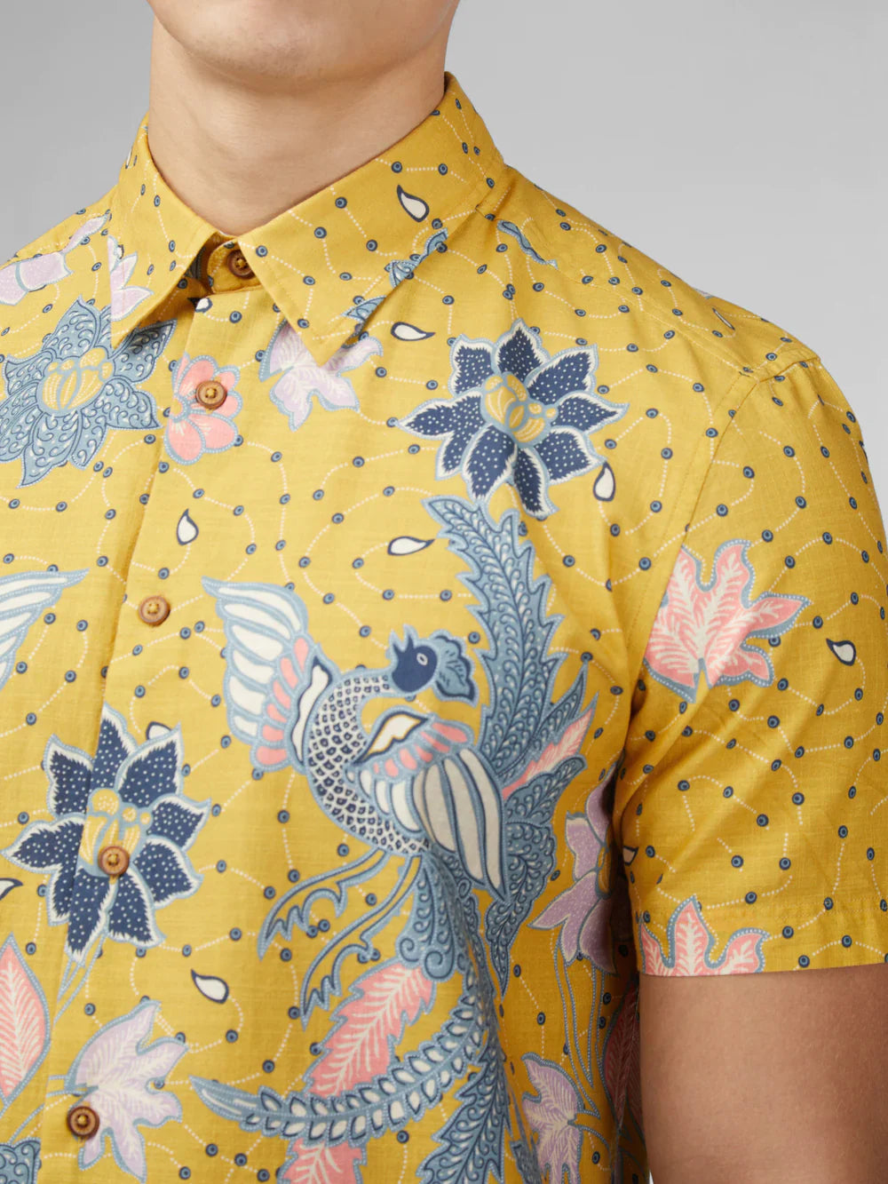 Yellow short-sleeved button-up shirt with intricate blue pink and white floral and bird patterns on textured fabric