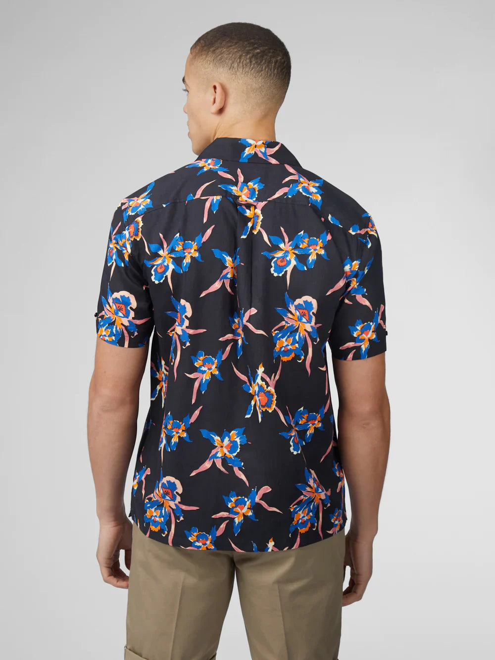 A man wearing a dark navy short-sleeved button-up shirt with vibrant blue and pink floral signature botanical print