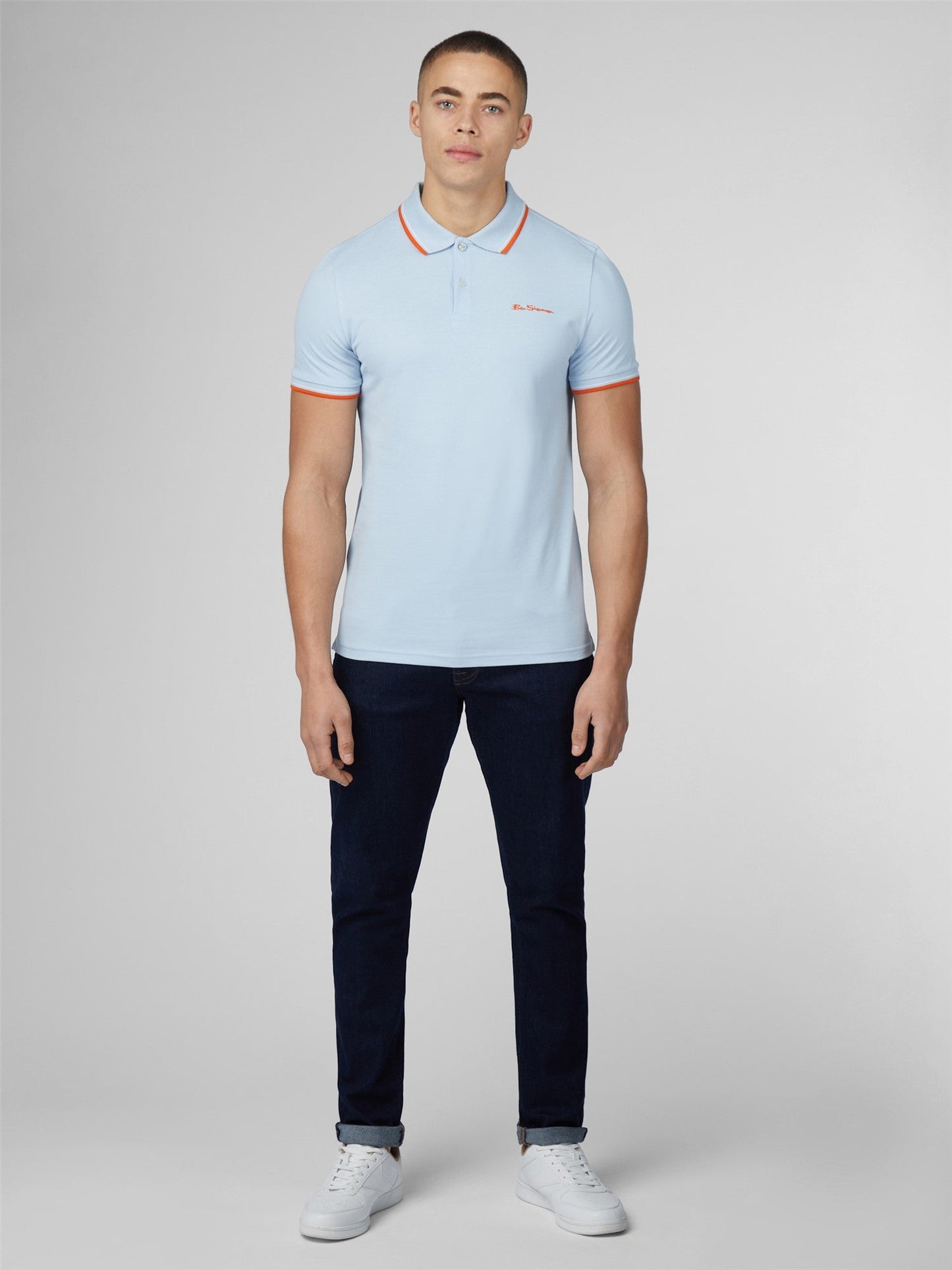 Light blue signature polo shirt with orange trim on collar and cuffs featuring small embroidered chest logo
