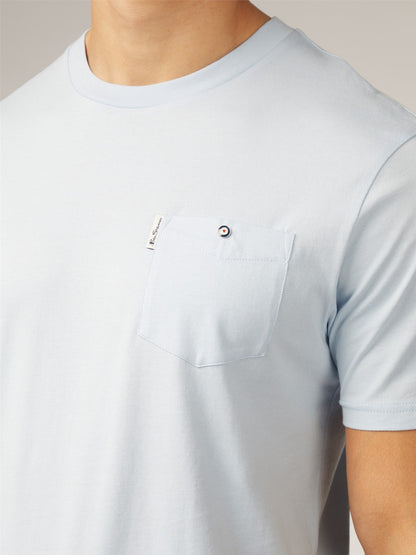 Light blue short-sleeved signature t-shirt with chest pocket and small black and white circular button closure