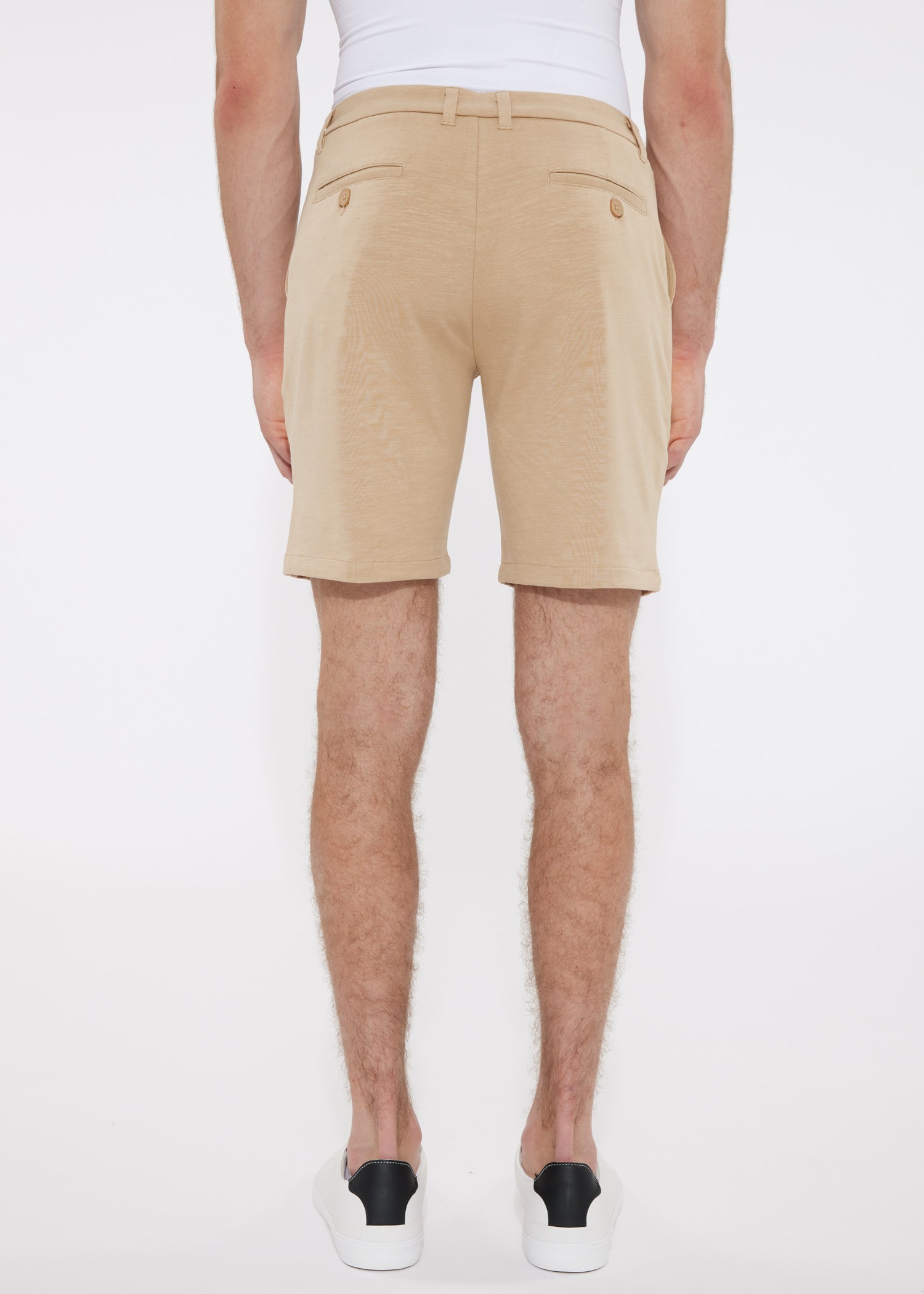 Beige solid stretch knit chino shorts with tailored fit and buttoned back pockets shown from the back side