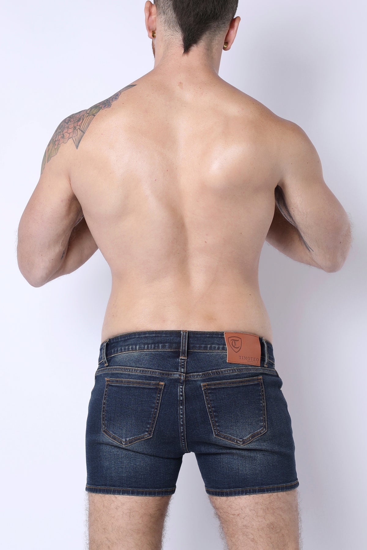 Dark blue denim soma 2.0 booty shorts shown from the back with a brown leather patch on the waistband
