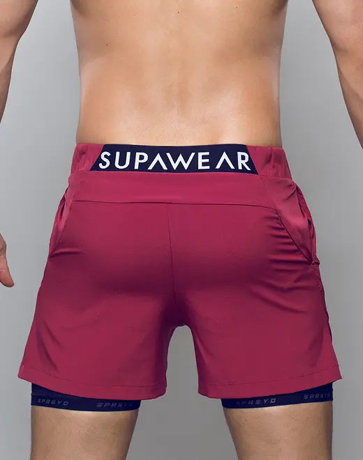 A pair of vibrant red spr max short athletic shorts with navy blue supawear logo waistband and matching compression shorts