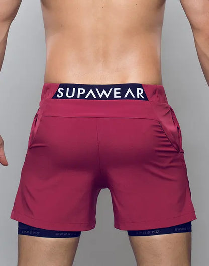A pair of vibrant red spr max short athletic shorts with navy blue supawear logo waistband and matching compression shorts