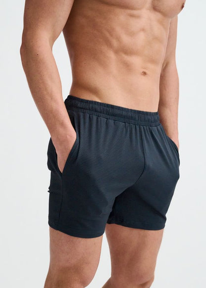 A person wearing dark grey, textured mesh gym shorts with an elastic waistband and side pockets.