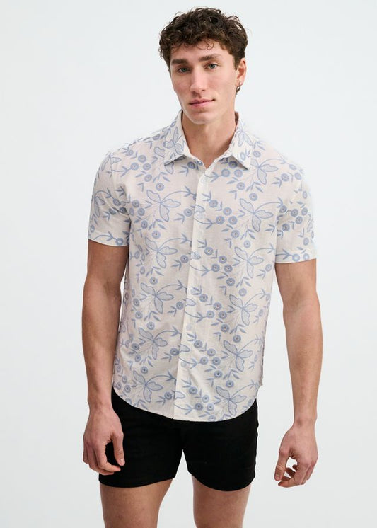 White short-sleeve button-down shirt with a sky blue floral eyelet print, worn over black shorts.